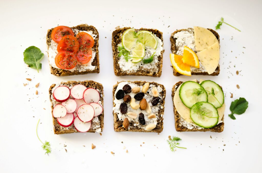 Six open-face rye bread toasts with cream cheese topped with tomatoes, cucumber, radish, nuts, and citrus for a diabetes-friendly diet