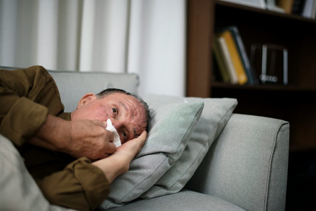 Older man on couch blowing his nose, showing effects of air pollution on seniors