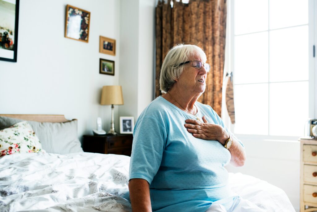 Woman with hand on chest due to chest discomfort, a symptom relevant to understanding calcified vs. soft plaque on cardiac CT scan results.