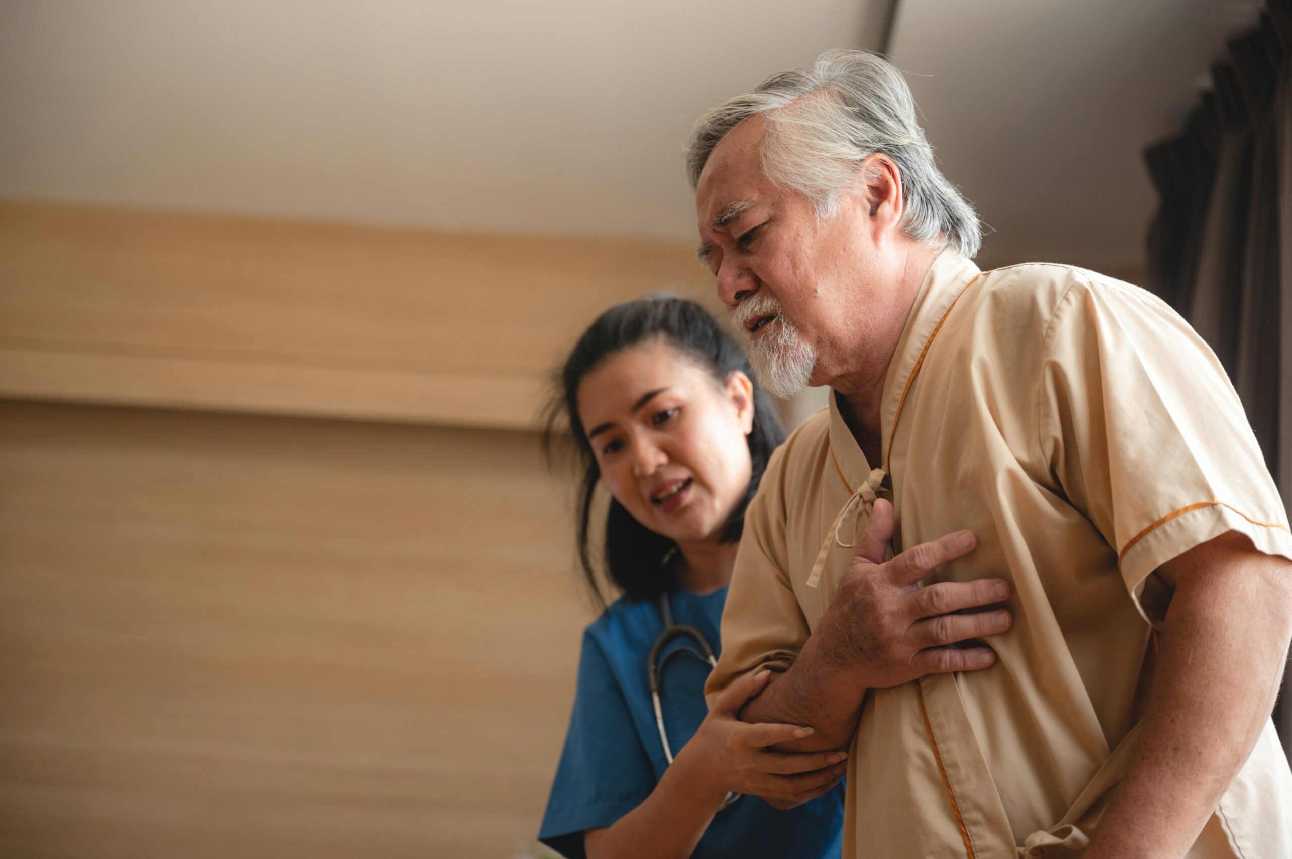 Elderly man clutching his chest in discomfort while a nurse supports his arm, illustrating symptoms related to soft plaque in arteries