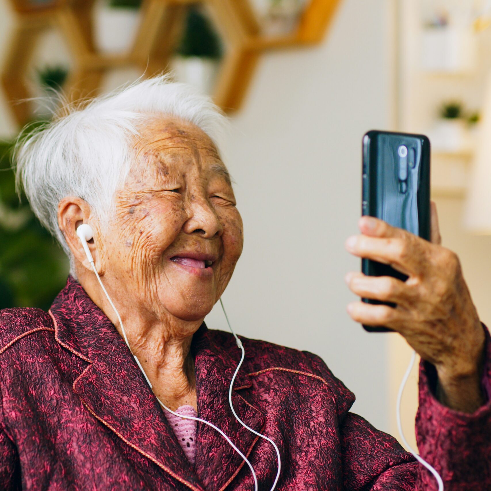 Elderly woman smiling during a telehealth video call on her smartphone, representing POD Health's chronic care management for Medicare members