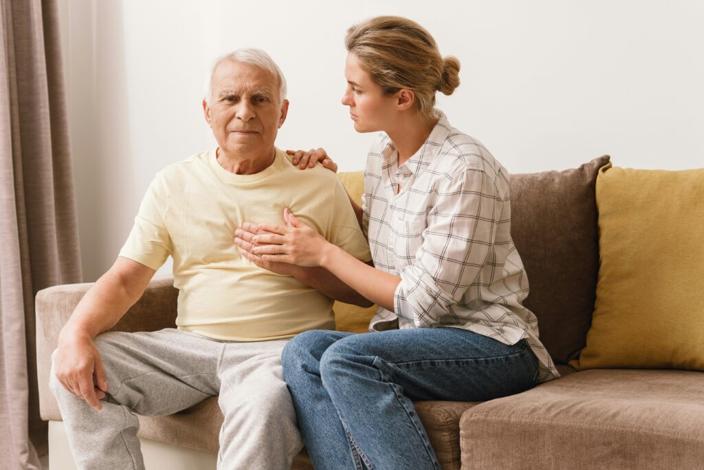 Older man with hand on his chest, supported by his daughter, showing signs of heart discomfort linked to chronic inflammation