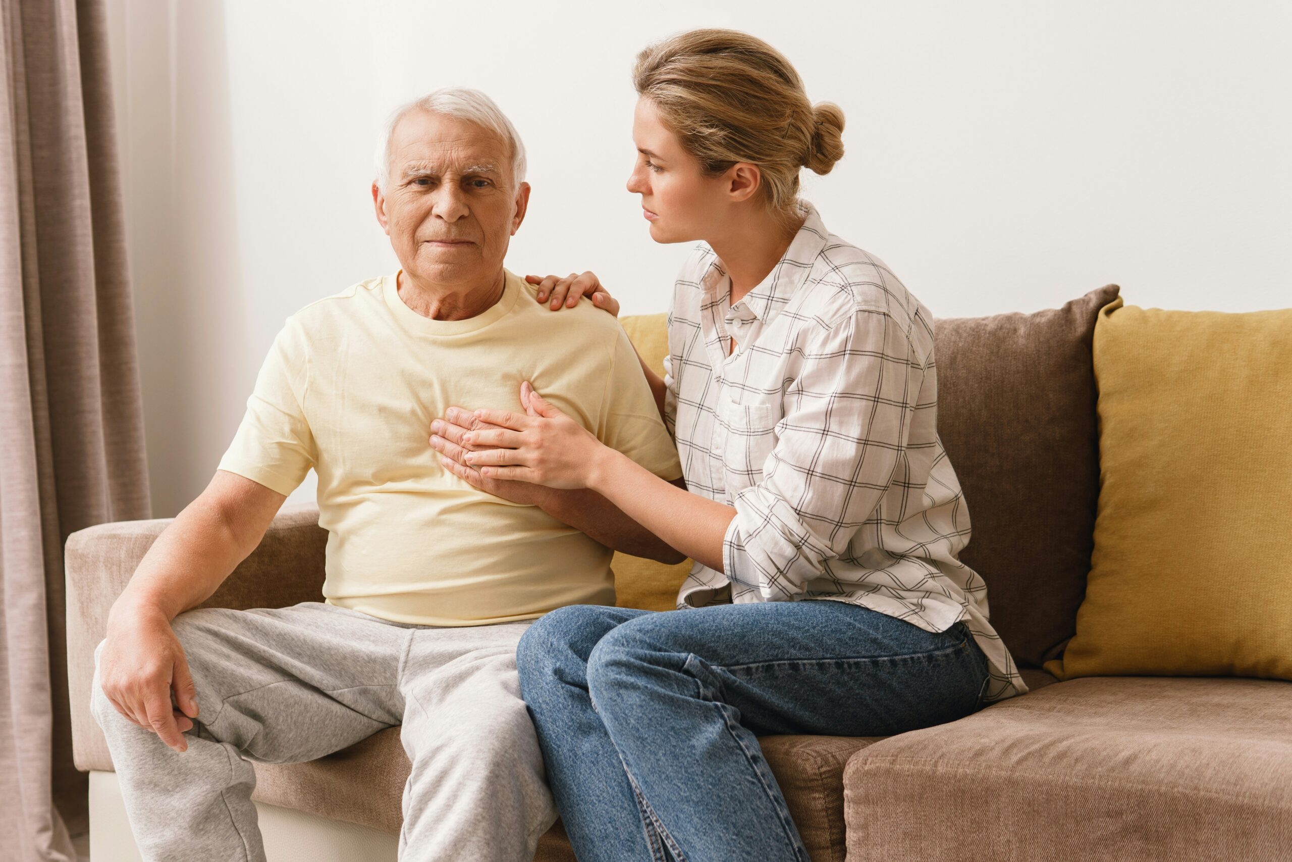 Older man with hand on his chest, supported by his daughter, showing signs of heart discomfort linked to chronic inflammation